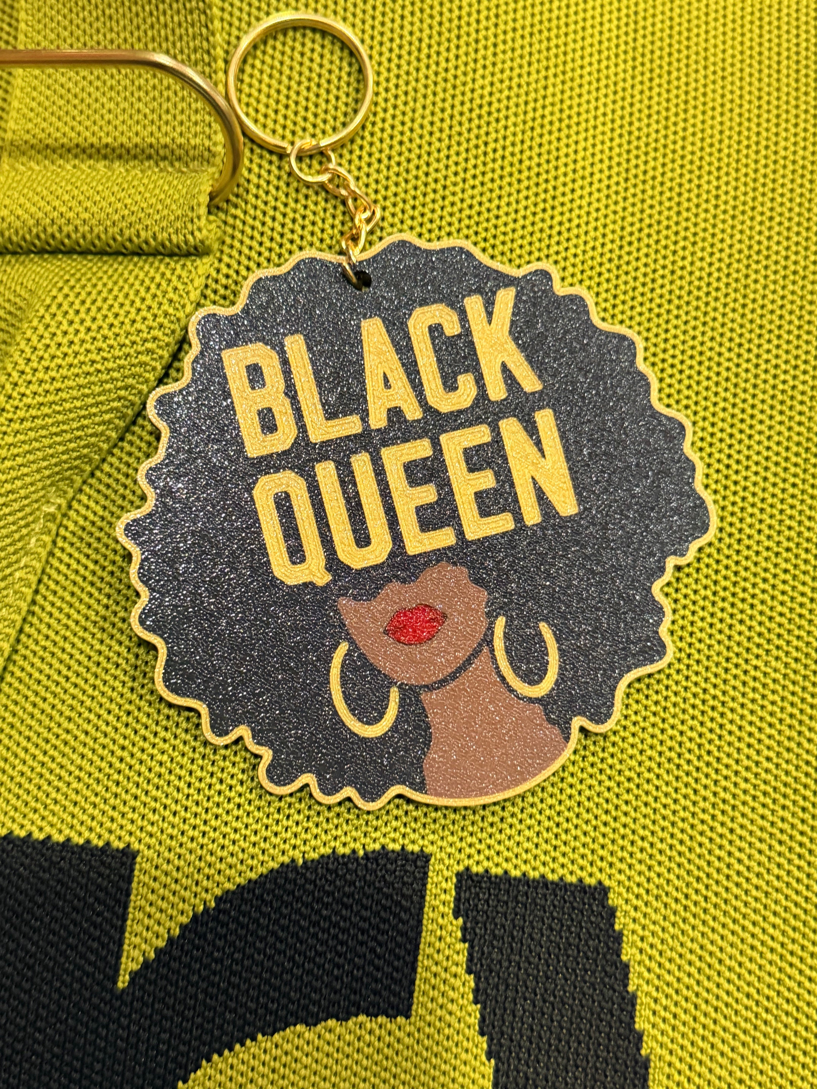 Black Queen Luxe keychain displayed on green fabric showing full design detail