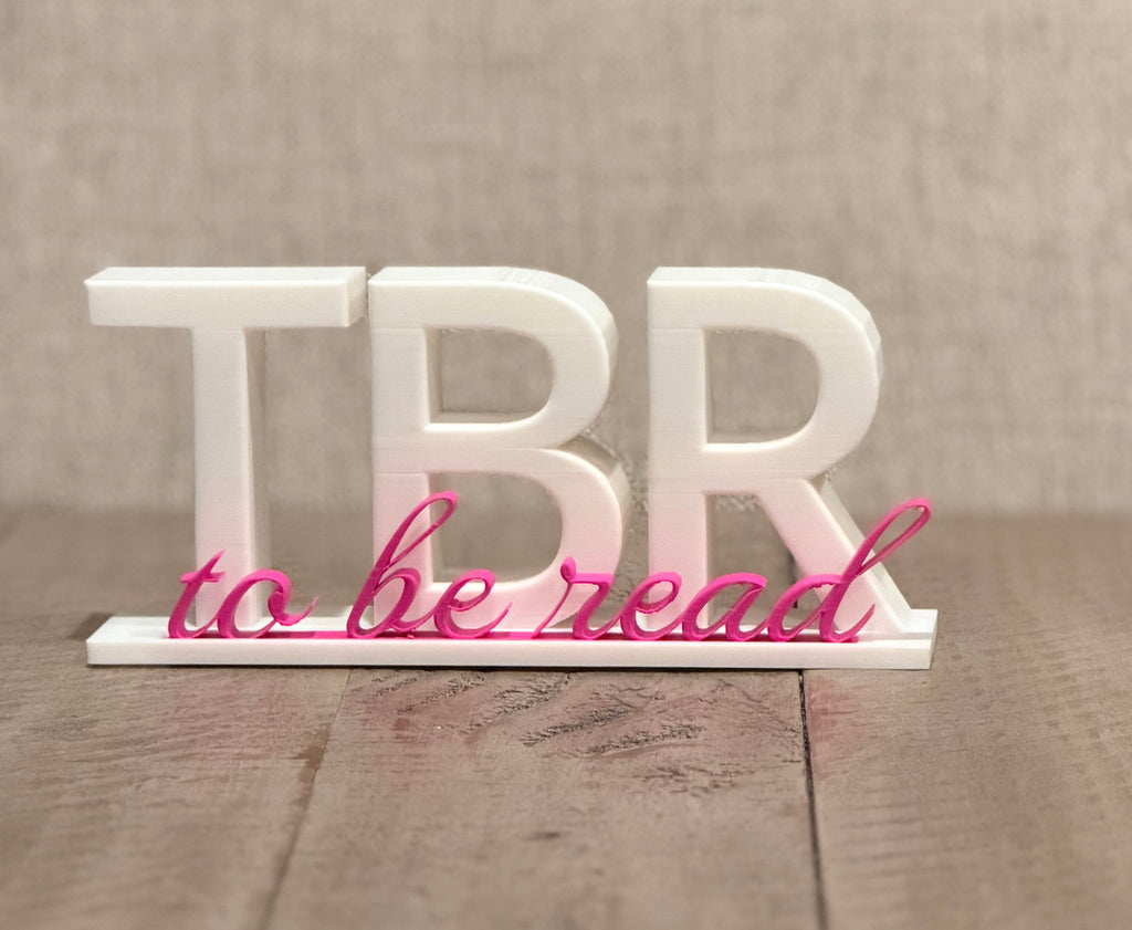 3D printed TBR To Be Read sign in white with hot pink cursive accent, displayed on wooden surface