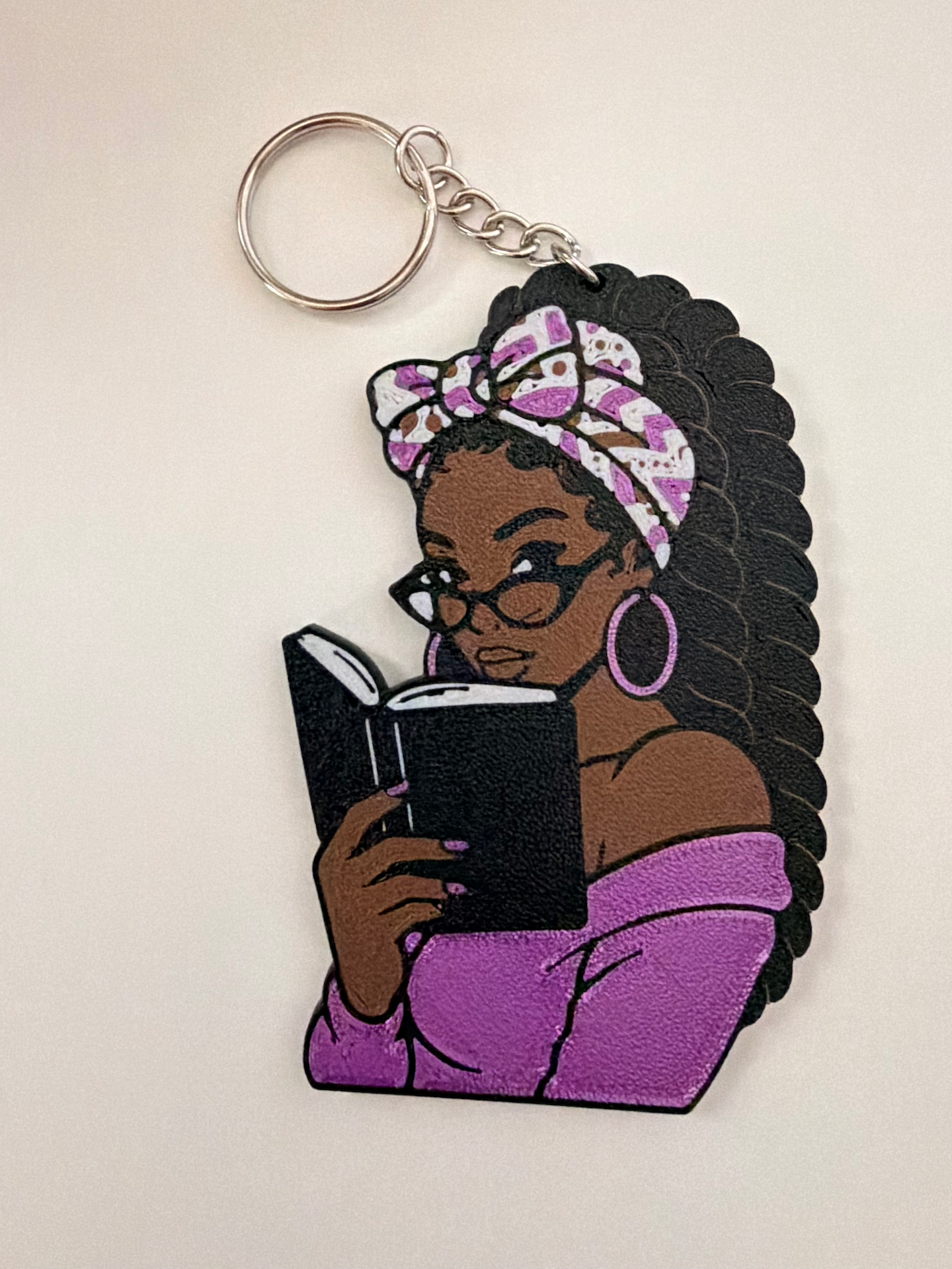 Bookish Black Girl 3D Bag Charm featuring a Black woman reading with glasses, hoop earrings, head scarf and natural hair