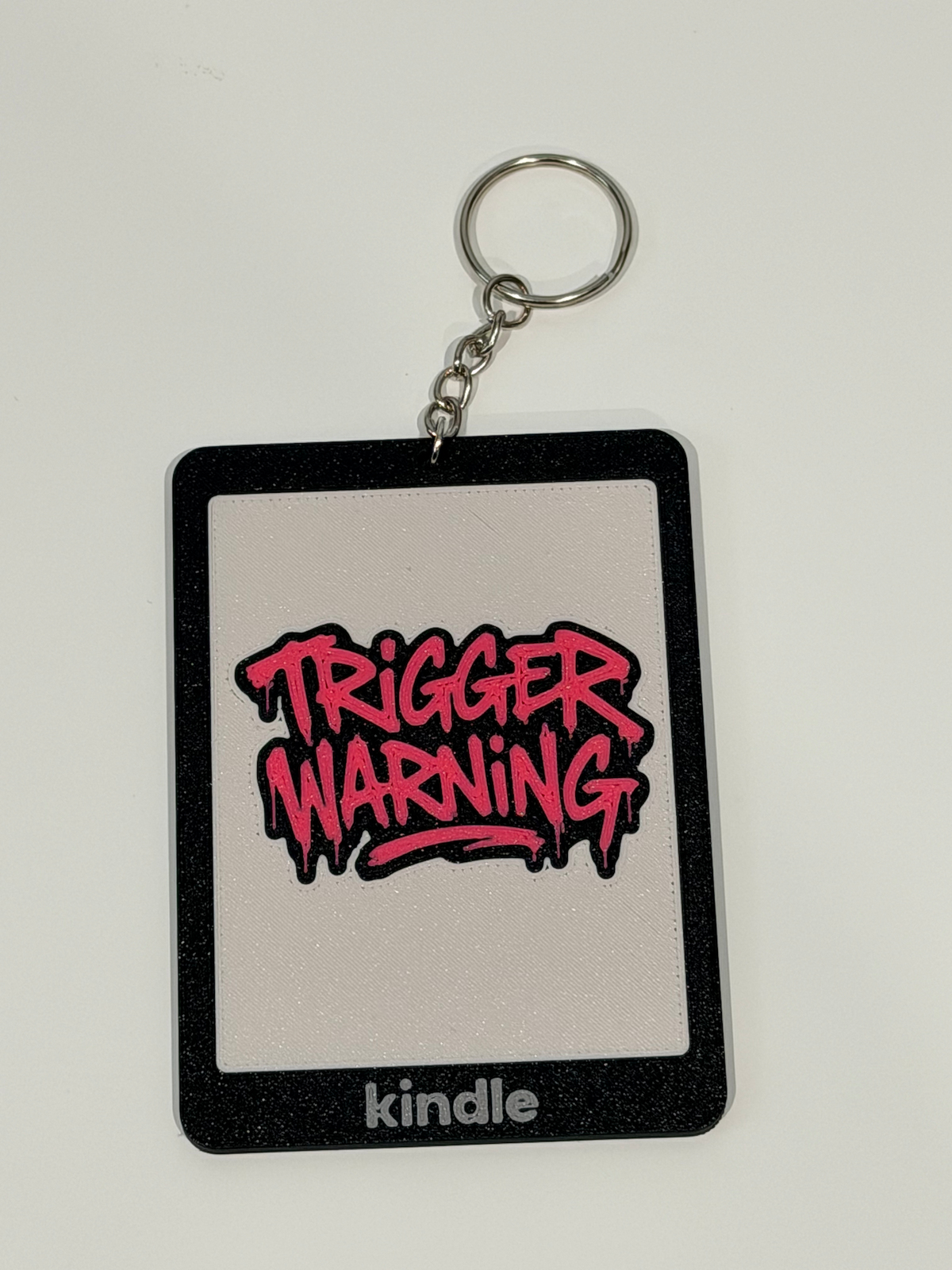 Trigger Warning Kindle bag charm, 3D printed with pink graffiti lettering on black and ivory Kindle design
