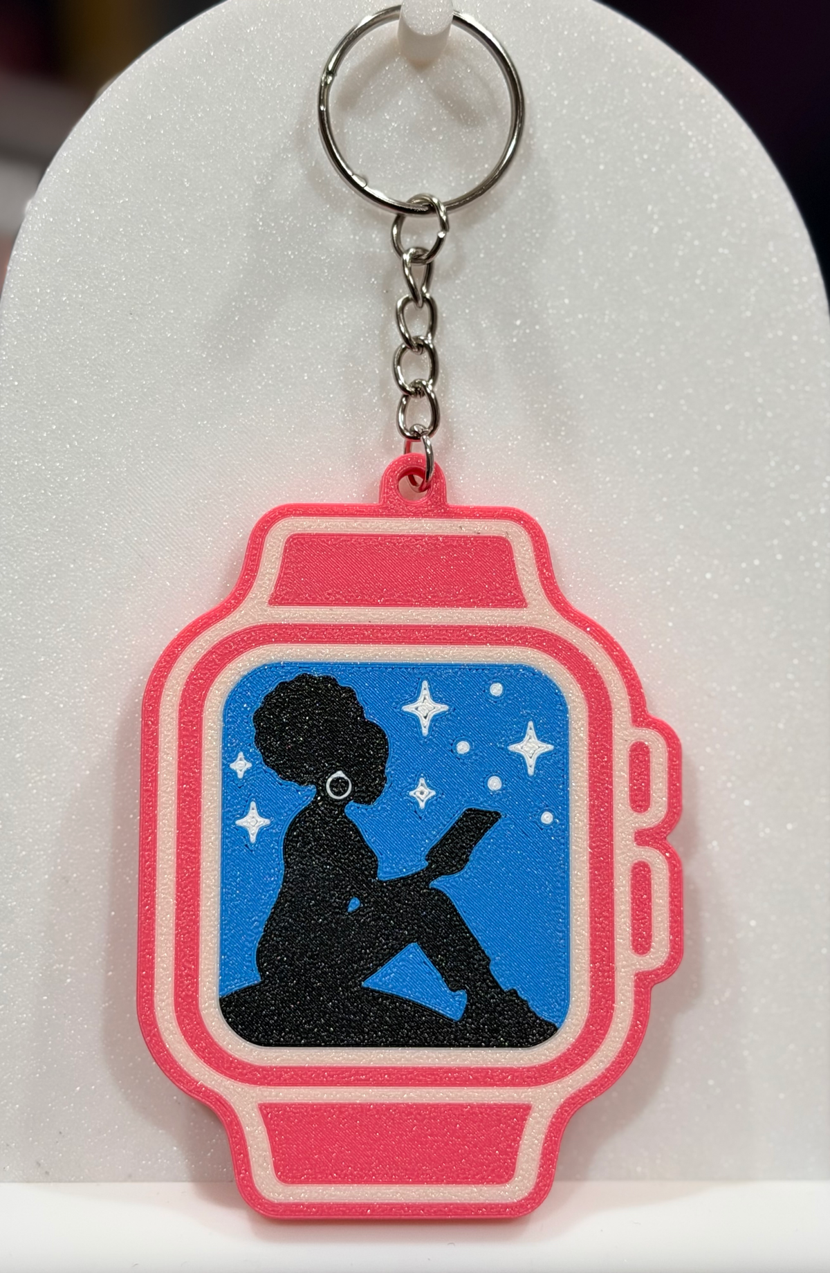 Pink watch-shaped keychain with a reader silhouette and white stars on a blue background